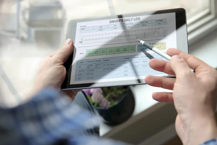 Truck driver checking electronic logbooks on a tablet after driving along Texas highway